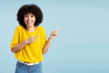 Kıvırcık saçlı ve sarı tişörtlü neşeli kadın, resmin sağ tarafındaki işaret parmaklarıyla bir ürün ya da servisi işaret ediyor. Reklam kavramı