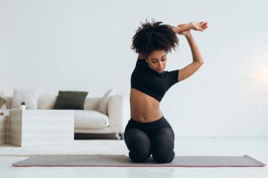 Sağlıklı bir yaşam tarzını benimseyen ve sağlığına odaklanan, rahat oturma odasında yoga yapan zinde siyah kadın.