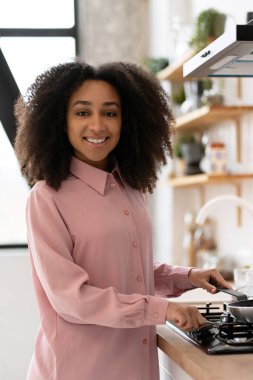 Genç bir kadın gaz ocağında tavada yemek pişiriyor, çağdaş aletlerle dolu şık ve modern bir mutfakta lezzetli bir yemek yapıyor.