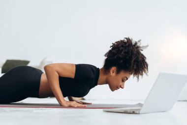 Spor kadını evde şınav çekiyor, laptopta spor yaparken spor videolarıyla uğraşıyor.