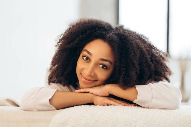 Kafasını ellerine dayayıp gülümseyen afro saçlı güzel siyah bir kadının portresi.