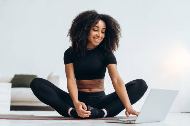 Bilgisayarda online özel ders izlerken yoga yapan sporcu bir kadın sporcu. Rahat dairesinde sağlıklı bir yaşam tarzının tadını çıkarıyor.