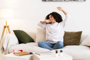 Genç serbest çalışan, uyandıktan sonra esniyor ve esniyor, oturma odasında rahat bir koltukta oturuyor, evde boş vakitlerin tadını çıkarıyor.