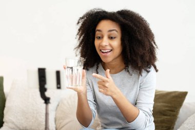 Heyecanlı genç bir kadın video kaydederken bir bardak suyu işaret ederek, online takipçileriyle susuzluk tutkusunu paylaşıyor.