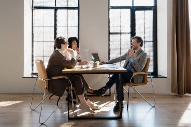 Üretken bir toplantıya katılan üç iş adamı, parlak ve modern ofis ortamında strateji ve fikirleri tartışıyor.