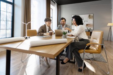 Mühendisler planları analiz ediyor ve dizüstü bilgisayar kullanıyorlar. Modern ofisteki minyatür rüzgar türbini modeli ile yenilenebilir enerji projesi üzerinde çalışıyorlar.