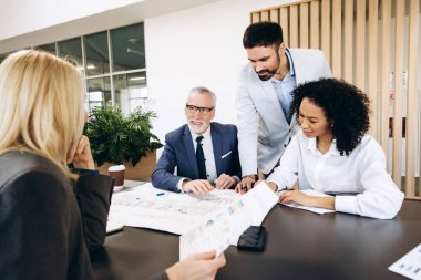 Proje üzerinde işbirliği yapan, planlar ve mali raporları analiz eden, modern ofis ortamında birlikte çalışan, takım çalışması ve uzmanlık sergileyen çok ırklı iş adamları. İş konsepti