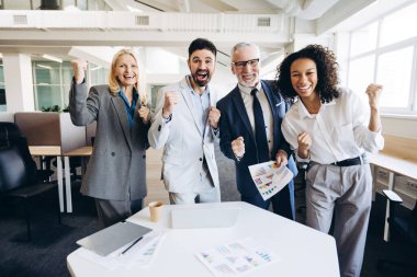 Modern ofis ortamında tamamlanmış projenin başarısını kutlarken gülümseyen çok uluslu bir iş ekibi heyacanlı bir şekilde takım çalışması ve başarının vücut bulmuş hali. Başarılı iş konsepti