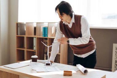 Minyatür bir rüzgar türbini modelini inceleyen Asyalı mühendis planlarla birlikte, sürdürülebilir enerji çözümlerini araştırıyor.