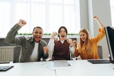 Çok kültürlü meslektaşlar zaferin tadını çıkarıyorlar, modern ofis çalışma sahasında silahlarını kaldırıyorlar, neşe ve takım çalışmasını ifade ediyorlar.