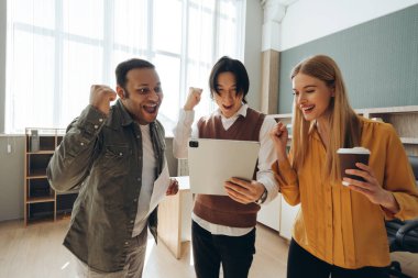 Çok ırklı iş adamları ofiste tablete bakarken başarıyı kutluyor, heyecan içinde yumruklarını kaldırıyor.