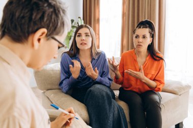 İki kadın bir koltukta oturup evdeki terapi seanslarında ilişki sorunlarını tartışıyor, destek ve rehberlik için psikoterapistleriyle ilişki kuruyorlar.