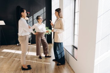 Üç iş kadını pencere kenarında bir proje üzerinde tartışırken, biri görüş açısını bir anlaşmazlığın ortasında belirtirken,