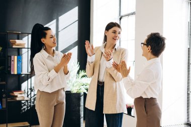 Çekici iş kadınları ofiste el çırpıyorlar ve başarılı bir proje veya başarıyı, takım çalışması ve destek göstererek kutluyorlar. İş konsepti