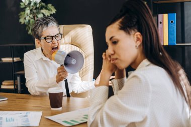 Sinirli üst düzey yönetici stresli bir iş gününde megafonla genç çalışana bağırıyor, iletişim sorunları, çatışma ve kötü liderlik gösteriyor.