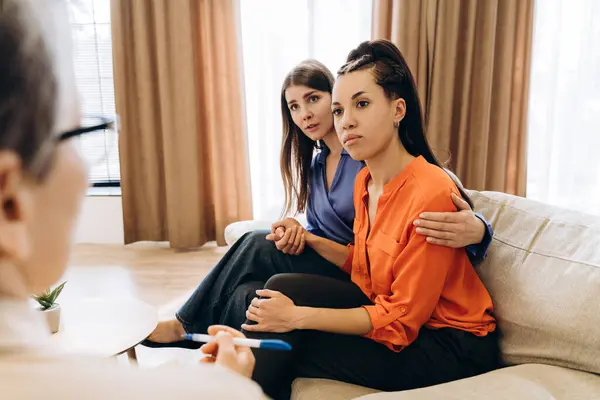 İki kadın bir psikologla terapi seansı sırasında el ele tutuşup birbirlerini teselli ediyorlar.