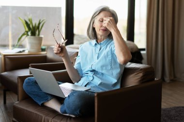 Gözlük tutan ve burun köprüsünü ovuşturan yorgun olgun bir kadın, kuru göz sendromu ya da bilgisayar çalışmasından sonra göz gerginliği çekiyor.