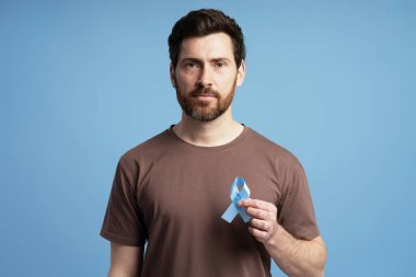 Prostat kanseri, kolon kanseri ve Addison hastalığı için açık mavi farkındalık kurdelesi tutan ciddi bir adamın portresi.
