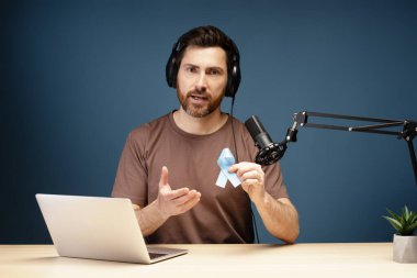 Radyo sunucusu, prostat kanseri farkındalığını sembolize ederken aynı zamanda mikrofon ve kulaklıkla podcast kaydı yapıyor.