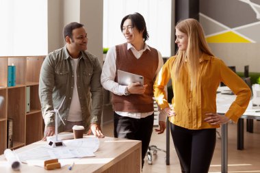 Modern ofiste rüzgar türbininin planlarını inceleyen çok ırklı mühendisler sürdürülebilir enerji çözümleri üzerinde işbirliği yapıyorlar.