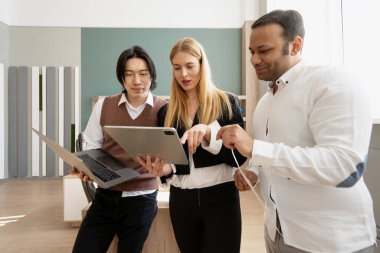 İş arkadaşları bir proje üzerinde birlikte çalışıyorlar, dizüstü bilgisayar ve dijital tablet kullanıyorlar, parlak bir ofis alanında fikirler ve stratejiler tartışıyorlar.