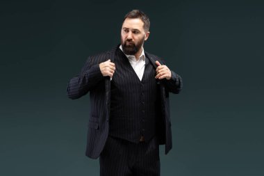 Kendine güvenen bir iş adamının portresi zarif ince çizgili takımını ayarlarken koyu bir arka planda poz vererek profesyonellik ve tarz yayıyor.