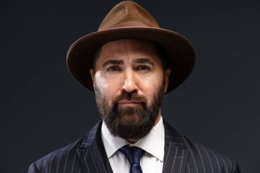 Takım elbise ve şapka giyen kendine güvenen bir iş adamının portresi, karanlık bir arka plana profesyonellik ve tarz yayıyor.