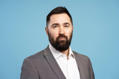 Takım elbise giyen ve mavi arka planda poz veren kendine güvenen bir iş adamının portresi profesyonelliği ve kararlılığı ifade ediyor.