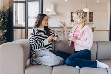 Evdeki oturma odasında birbirleriyle konuşan, ellerinde yoğurtla gülümseyen iki genç kadının portresi. İnsan yaşam tarzı, arkadaşlık kavramı