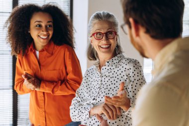 Çok ırklı iş kadınları ve işadamları, gülümseyen ve konuşan, ofiste yapılan gayri resmi görüşmeler, takım çalışması, işbirliği, çeşitlilik ve işyerlerine dahil etme. Takım çalışması konsepti
