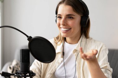 Gülümseyen kadın ses kaydını stüdyo mikrofonu ve kulaklıkla yapıyor, evden podcast yaratıyor