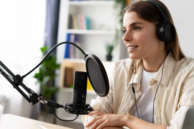 İçerik yaratıcısı mikrofon kayıt podcast veya online radyo şovuna konuşuyor. Ev stüdyosunda kulaklık takıyor.