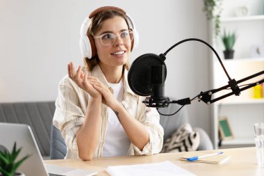 Podcaster ses içeriği yaratıyor, mikrofona konuşuyor, kulaklık takıyor, evden çalışıyor.