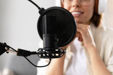 İçerik oluşturucu profesyonel bir mikrofon ve kulaklık kullanarak bir podcast kaydediyor, ses kalitesine odaklanıyor ve dinleyicileri kendine çekiyor