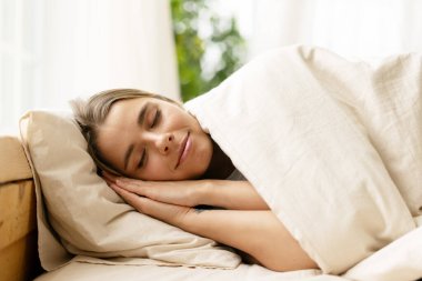 Genç bir kadın rahat bir yatakta mışıl mışıl uyuyor, rahat bir battaniyeyle örtülmüş, evde huzurlu ve huzurlu bir sabah geçiriyor.