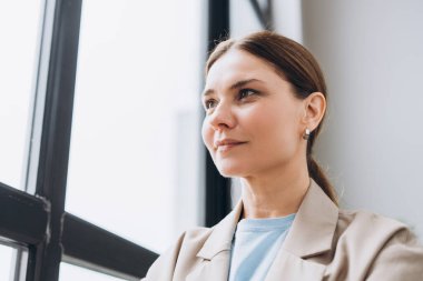 Düşünceli iş kadını pencereden dışarı bakıyor, gelecek projeleri düşünüyor ve büyüme ve başarı için fırsatlar öngörüyor.