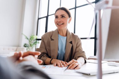 İş kadını gülümseyip ofisteki meslektaşıyla yenilenebilir enerji projesini tartışıyor.