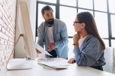 İş arkadaşları proje raporları üzerinde işbirliği yapıyor, verileri analiz ediyor ve modern ofis ortamında stratejileri tartışıyorlar.