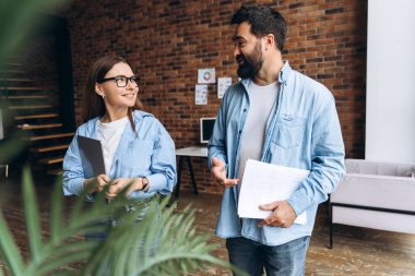 İş ortakları modern bir çatı katında yürüyor, proje stratejisini tartışıyor ve başarı için yenilikçi fikirler üzerinde işbirliği yapıyorlar.