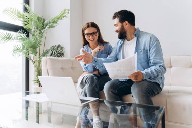 İki mimar bir video konferansında bir projeyi tartışıyorlar, dizüstü bilgisayarın ekranını gösteriyorlar ve planları tutuyorlar.