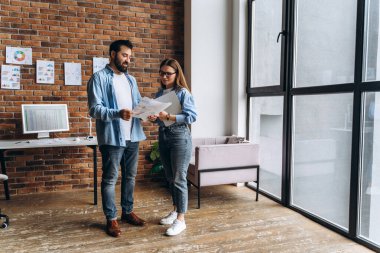 İki iş ortağı, modern ofiste mali tabloları analiz ediyor. Tablolar duvarda asılı duruyor.