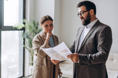 İş adamı ve işkadını basılı çizelge ve grafikleri inceleyerek, ofis ortamındaki mali performans ve pazar eğilimlerini tartıştılar
