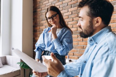 İki genç iş ortağı bir projeyi tartışıyorlar. Belgeleri analiz ediyorlar ve modern bir ofiste yeni fikirler üretiyorlar.
