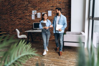 İş ortakları belgelerini tutuyor, modern ofiste yürüyor, iş tartışıyor ve fikir alışverişinde bulunuyorlar.