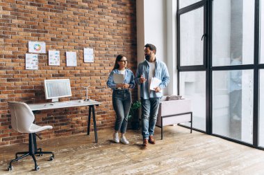 Modern ofiste yürüyen ve pazarlama stratejisini tartışan iki iş ortağı tuğla duvar ve geniş pencereli