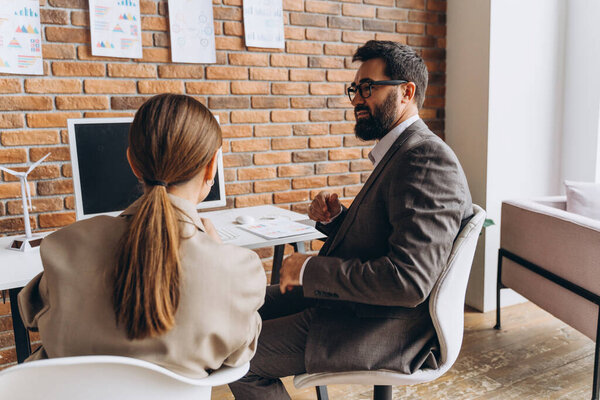 Business partners discussing renewable energy project in office with computer and miniature wind turbine and solar panel