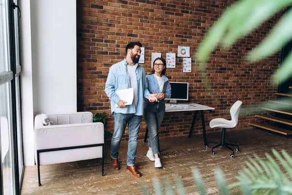 İki meslektaş modern bir ofiste yürürken, etrafı tuğladan duvarlarla çevrili, parlak, havadar bir dekorla çevrili bir şekilde iş konuşuyorlar.