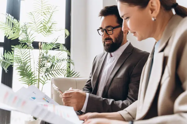 İşadamları kağıt belgeler ve cep telefonları üzerinde finansal çizelge ve grafikleri analiz ediyor, ofiste birlikte çalışıyorlar.