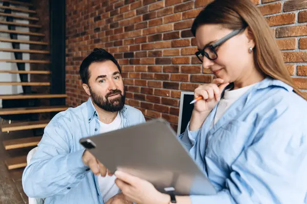 Modern bir ofiste duvarları açık bir tablet kullanarak iş, fikir alışverişi ve bir proje üzerinde işbirliği yapan iki iş arkadaşı.
