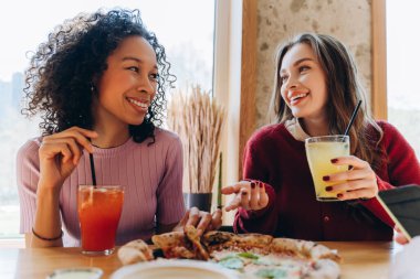 Lezzetli pizzanın ve sıcak restoranda içkinin tadını çıkaran iki neşeli genç bayan. İletişim, arkadaşlık kavramı